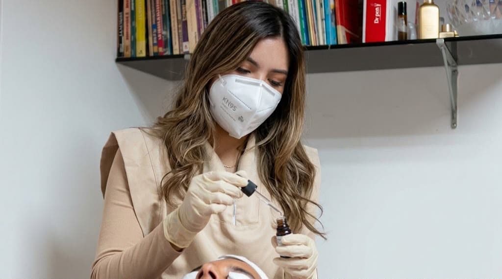 Mujer aplicándose crema facial frente a un fondo cálido